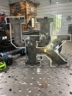 Large custom plasma-cut metal letter displayed in a fabrication workshop.