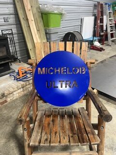 Blue powder-coated metal Michelob Ultra sign displayed in a metalworking workshop.